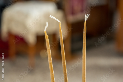 Three candles with burnt tips stand in soft focus on a table with blurred furniture in the background during daytime