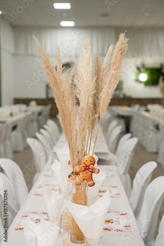 Table set up for a festive event with decorative plants and a gingerbread figure at a venue in the evening