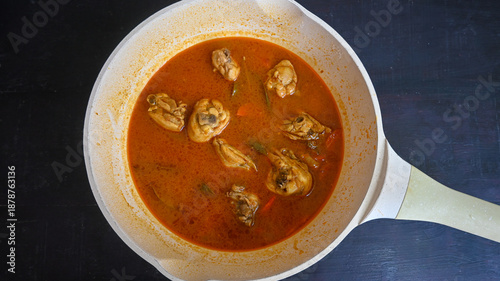 Overhead view of spicy chicken curry simmering in a white ceramic pan on a dark background