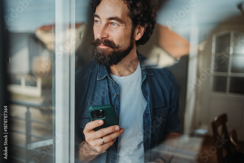 Fotografie Man holding phone contemplating looking out window