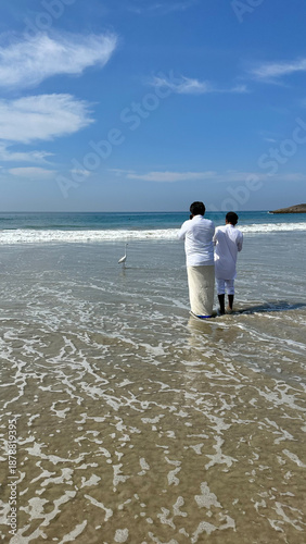 Photography Two Indian men take a photo of a white egret on the beach.