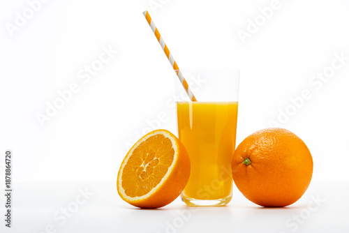 Fresh orange juice in glass with whole and sliced oranges beside it on a plain background