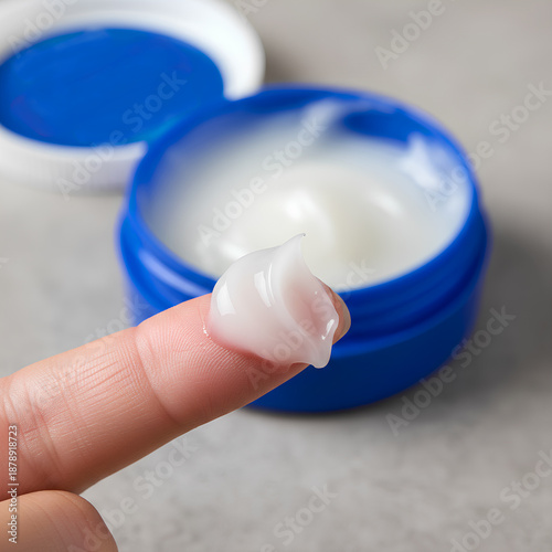 Wallpaper Mural Close-up of a person's fingers holding a dollop of white moisturizing face cream gel with an open blue cosmetic jar in the background, skincare and beauty routine concept Torontodigital.ca