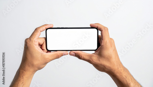 Hands holding a smartphone horizontally with a blank white screen for copy space