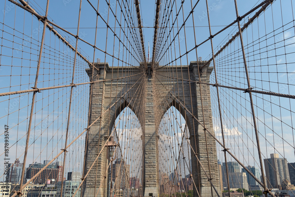 Obraz premium The Brooklyn Bridge, built in 1883, is the first suspension bridge constructed of steel and overlooks the skyscrapers of Manhattan, the Big Apple.