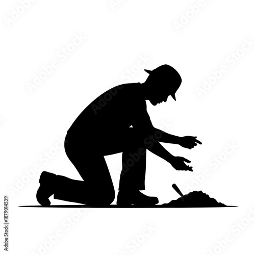 Silhouette of a man kneeling and working with soil outdoors.