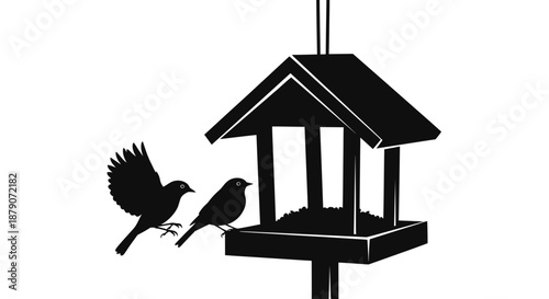 A black silhouette of two birds interacting with a hanging bird feeder