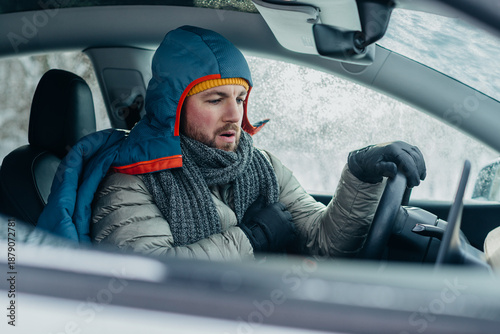 Fotografie Cold man stuck in electric car during winter storm