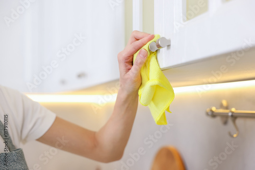 Foto Woman wiping cabinet handle with microfiber cloth in kitchen, closeup