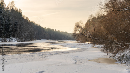 Εκτύπωση καμβά Winter river bend at golden dusk with snow covered banks and forest reflections,