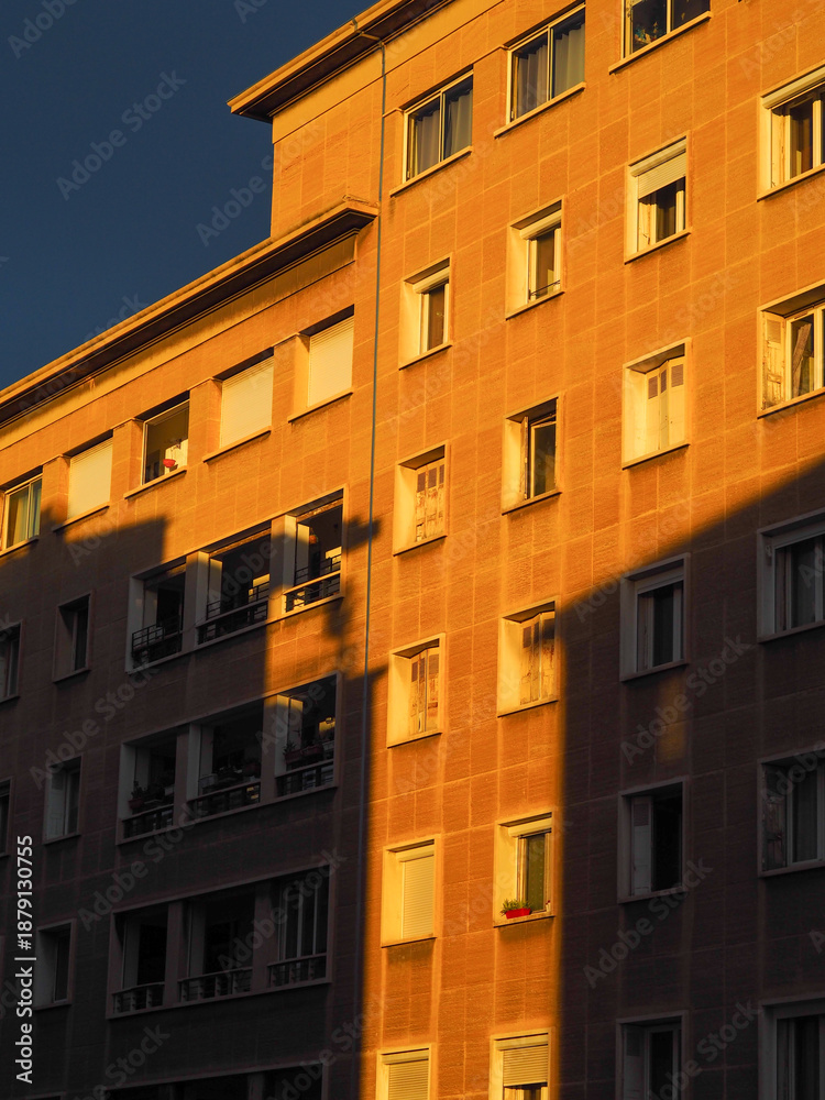 Fototapeta premium Façade d'immeuble moderne à Marseille sous la lumière dorée du lever de soleil, jeu d'ombres géométriques