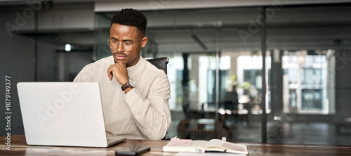 Obraz na płótnie Busy professional African business man company employee, young male businessman looking at computer thinking on online investment or software technology using laptop working at office