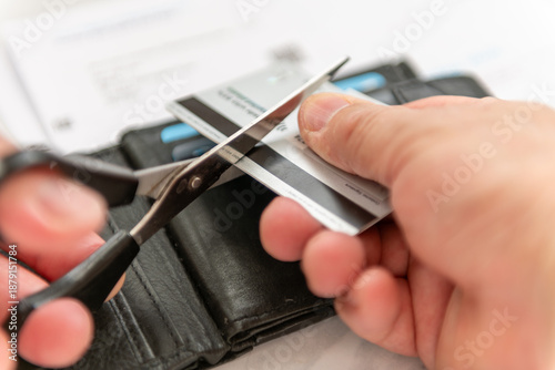 Obraz na plátně A close up of a person using a pair of scissors to cut up a bank credit card with a purse and credit card bills in the background