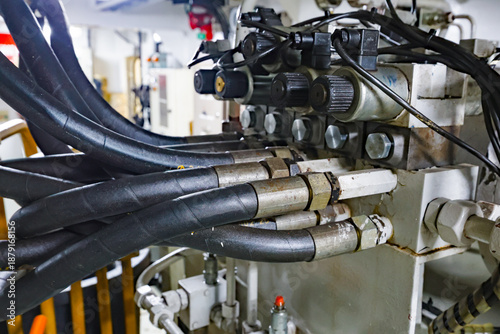 Hydraulic control unit with high-pressure hoses, fittings and valves inside an industrial engine room, showing fluid power and mechanical engineering system.
