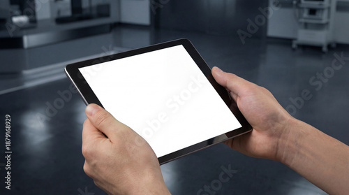 Hands holding a tablet displaying a blank white screen, offering ample copy space for medical data or research results within a modern hospital or laboratory environment