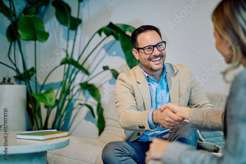 Foto Business man and woman shaking hands in a casual office setting, smiling, confir