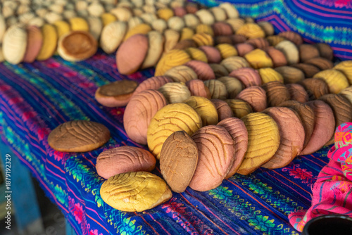 Vanilla, chocolate, and strawberry conchas on a colorful tablecloth at a blue wooden bread stall. Traditional bakery. Petatlan, Guerrero, Mexico. cochitas