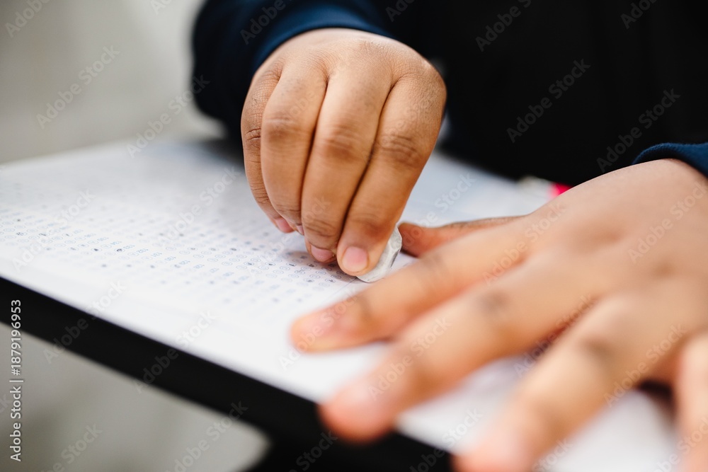 Obraz premium Close-up of hands erasing on paper. Focus on eraser and paper. Hands of a person erasing. Eraser and paper interaction. Erasing on paper close-up. Young student erasing answer in exam. Exam in school.