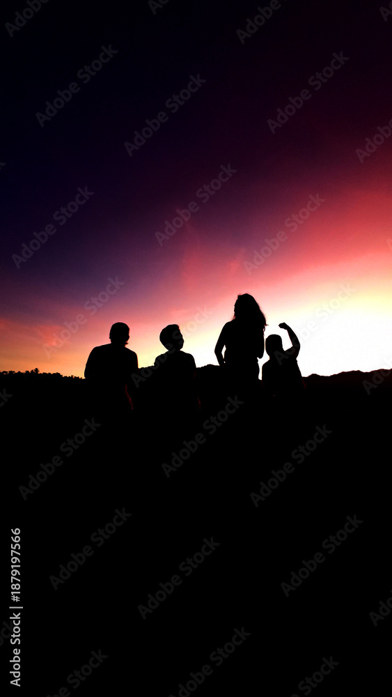 Fototapeta premium Silhouette of best friends, together watching colorful sunrise sky on the background. Romantic pink sky and dark cloud with four happy women celebrating life together.