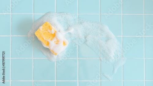 Fotografía Yellow sponge with soap suds on light blue tiled backgrond