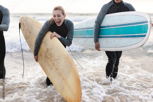 Canvas Print Two people in wetsuits carrying surfboards at the beach