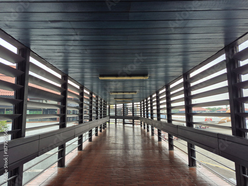 Classic airport terminal connecting corridor with wooden ceiling, ventilated wooden walls, and brown tile floor, designed for natural airflow, comfort, and traditional architectural style.