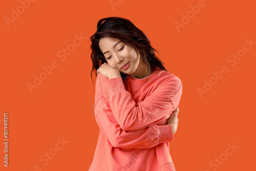 Tableau sur toile Young Asian woman hugging himself on orange background