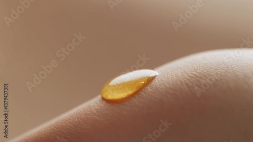 Macro close-up of a golden drop of cosmetic oil or serum resting on smooth human skin, symbolizing hydration, beauty, and wellness.