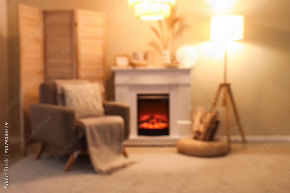 Obraz premium Blurred view of cozy living room with fireplace, armchair and glowing lamps