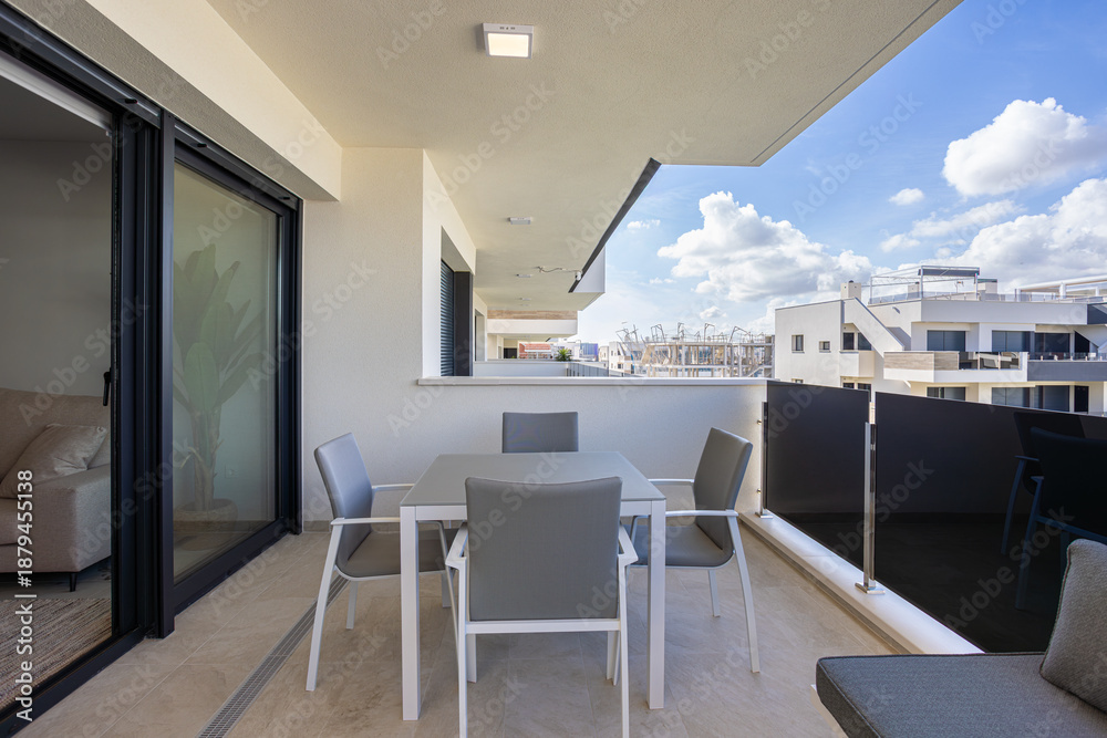 Naklejka premium Covered modern balcony with dining table and scenic residential building view