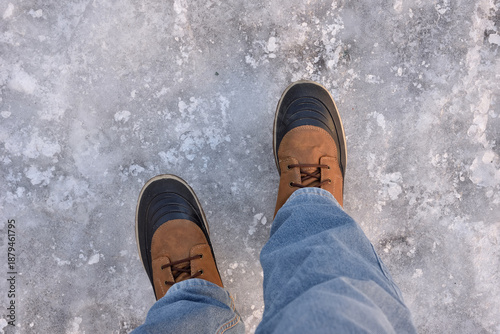 Man wearing boots and jeans walking on icy and slippery sidewalk in winter. Dangerous for walking! Top view. 