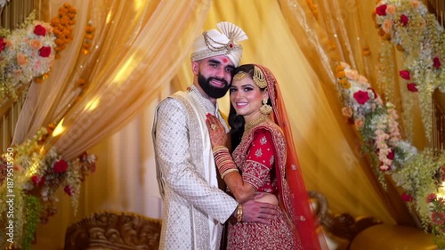 Romantic Indian wedding couple in traditional attire posing at luxury ceremony venue with warm golden decorations.