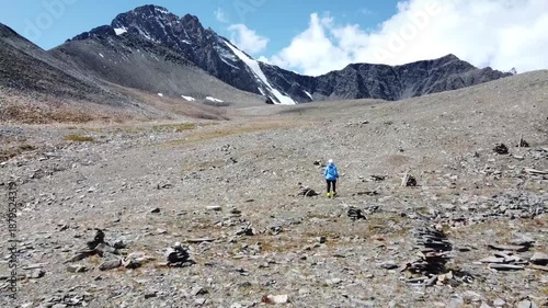 A girl walks along a mountain range. There are snowy mountains in the background. Active recreation