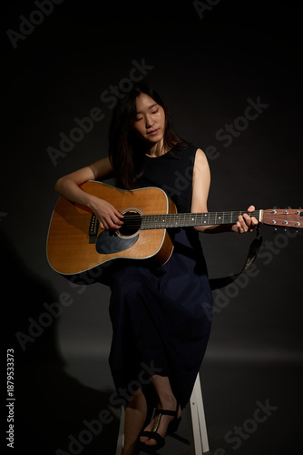 Talented Asian guitar player performing in dark room, selective focus on instrument