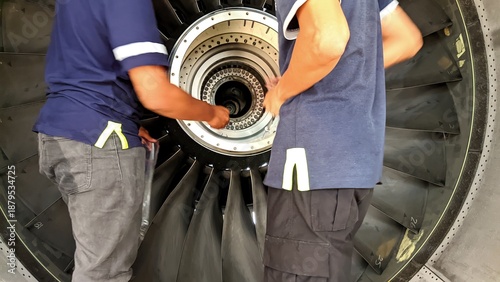 Aircraft maintenance technicians performing detailed inspection and maintenance on a turbofan jet engine inside an aircraft hangar