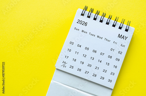 White spiral desk calendar for May 2026 on yellow background with modern presentation and space for text.