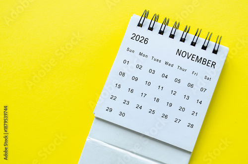 White spiral desk calendar for November 2026 on yellow background with clean framing and space for text.