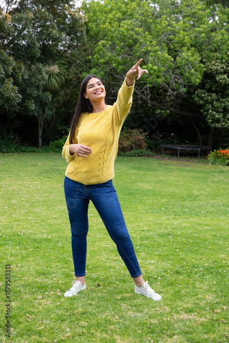 Canvas-taulu Woman standing on lawn wearing mustard sweater and jeans pointing in garden with
