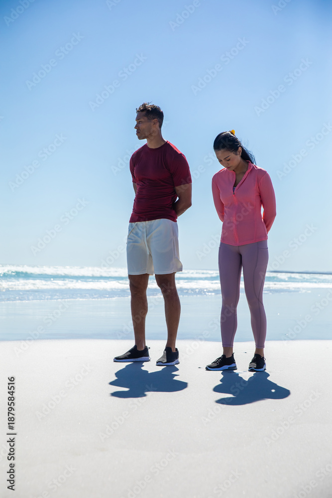 Fototapeta premium Diverse friends standing on sandy beach feeling ocean waves on wet sand in athletic footwear
