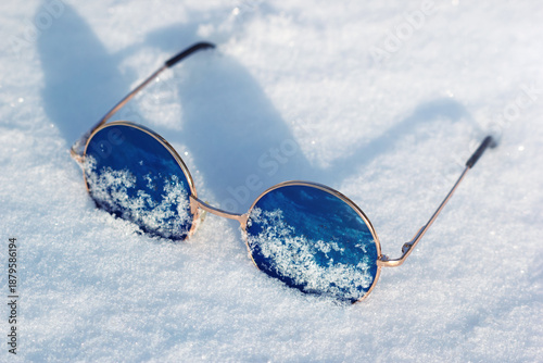 The cool blue lens sunglasses fallen in snow. The stylish eye protection in winter season and bright white snow.