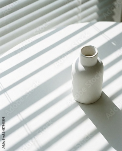 White ceramic vase with harsh striped shadows from window blinds. Aesthetic minimalist still life background.