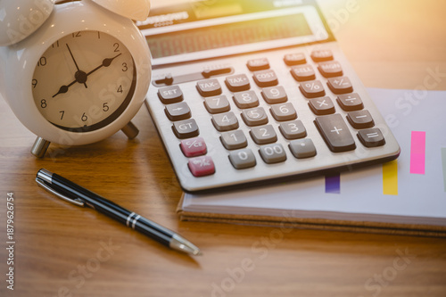 Calculator and alarm clock notebook with pen on wood table with blurred bokeh background appointment and business meeting, representing time management business planning concept