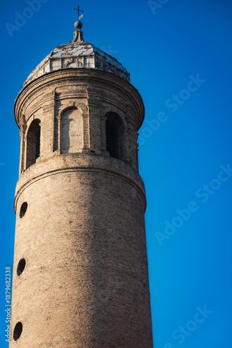 Detail of a historic cylindrical brick bell tower with arched windows and a dome top against a clear blue sky in Ravenna