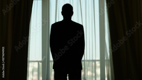 Guy stay against fabric draperies,, quickly stretch out hands holding edges and open curtains. Silhouetted half length view from back, slow motion shot. Man wear casual suit