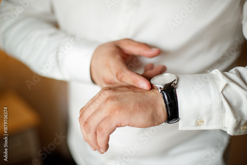 A man in a suit is wearing a watch and adjusting his jacket. The image has a blurry quality, which gives it a sense of motion and action. The man's focus on his watch