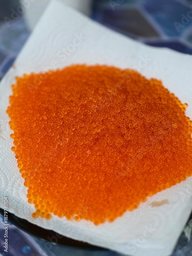 High-angle close-up of fresh red caviar (salmon roe) drying on a white paper towel.