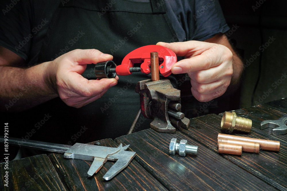Fototapeta premium A person works with a pipe cutter to cut a metal pipe. Various tools are placed on the workbench, showing a busy workshop setting. The activity takes place in daylight