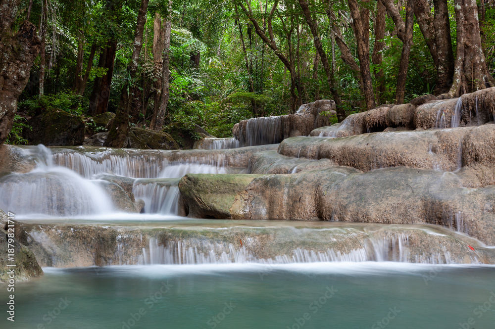 Naklejka premium Erawan Falls cascading over rocky ledges in the lush Erawan National Park. Tropical greenery surrounds the flowing water. Located in Kanchanaburi, Thailand, in a serene forest landscape.