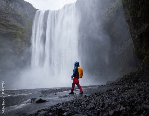 Hiker getting wet as enjoying views on big beautiful waterfall in front of him, Iceland