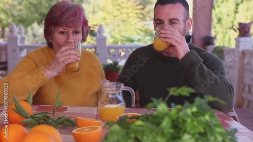 Mother and son having breakfast with freshly squeezed orange juice surrounded by oranges in a country house surrounded by nature